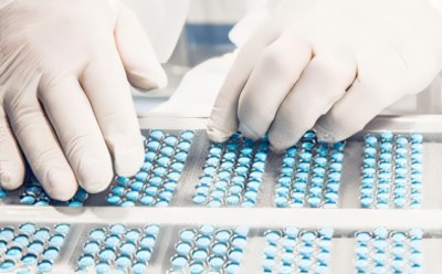 Pill inspection 制药或医疗生产设施。其中一人正穿着防护服,操作装满蓝色胶囊的托盘。