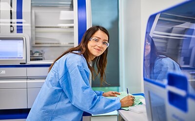 Expert mRNA analytical development services Female scientist in a blue lab coat completing paperwork on the lab bench of the molecular contract testing laboratory.